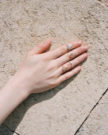 Close-up of a hand resting against a rough stone wall, adorned with diamond rings