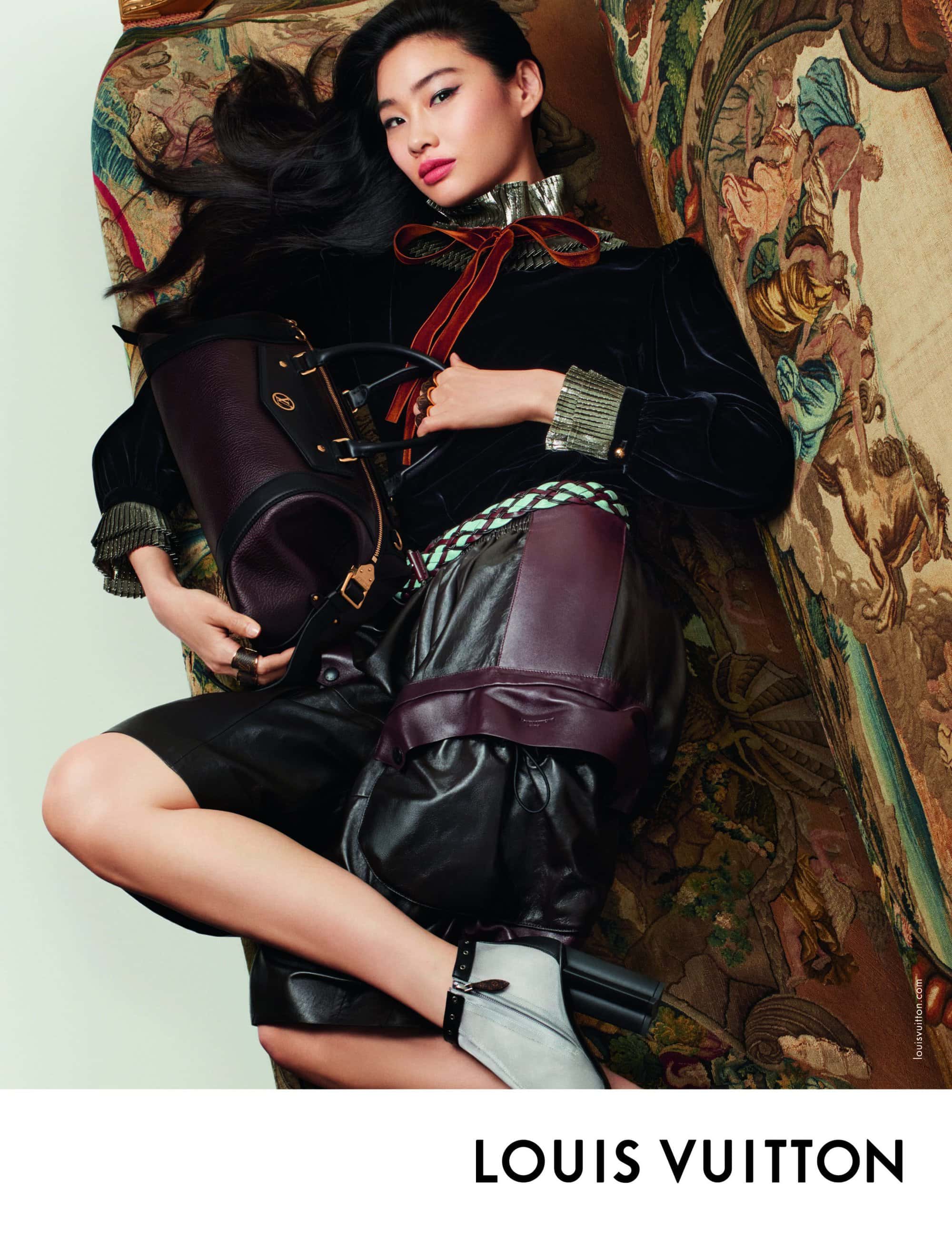 Model Hoyeon in black velvet top and leather trousers reclining on a tapestry sofa holding a dark leather handbag for Louis Vuitton.