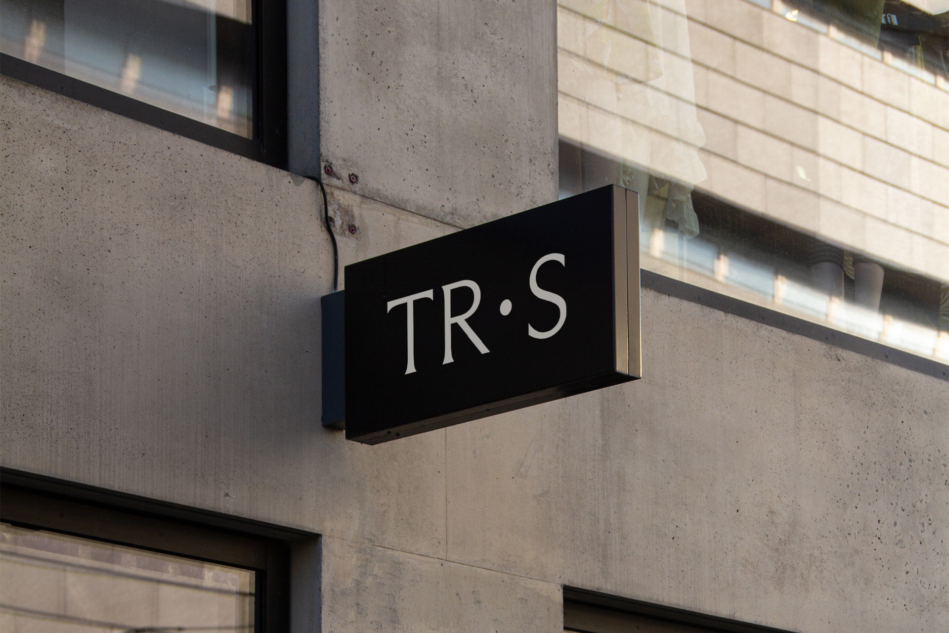 Black rectangular sign with white lettering mounted on a modern concrete building exterior wall