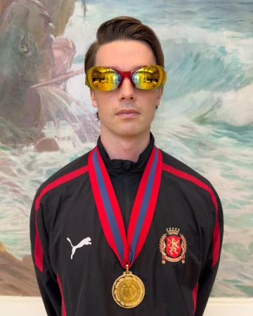 Man wearing mirrored yellow sunglasses and a black track jacket with a gold medal against an ocean mural