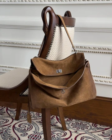 Brown suede shoulder bag draped over the back of an antique wooden carved chair in a classic room