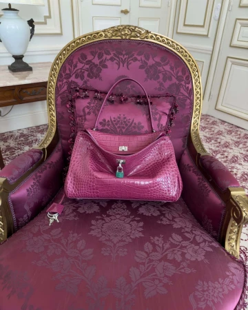 Pink exotic leather handbag resting on an ornate magenta damask armchair inside an elegant room