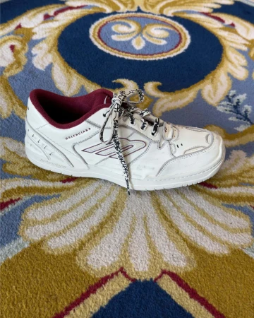 Balenciaga white sneaker with burgundy lining and patterned laces on a blue and yellow patterned carpet.