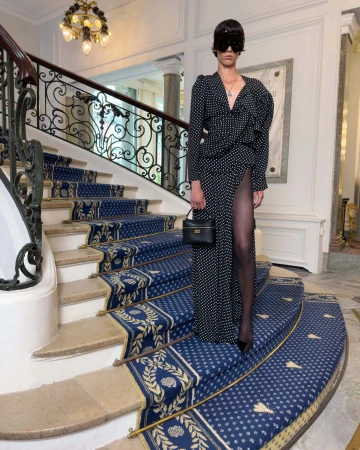 Model wearing black polka dot dress and sunglasses standing on a grand staircase with blue carpet