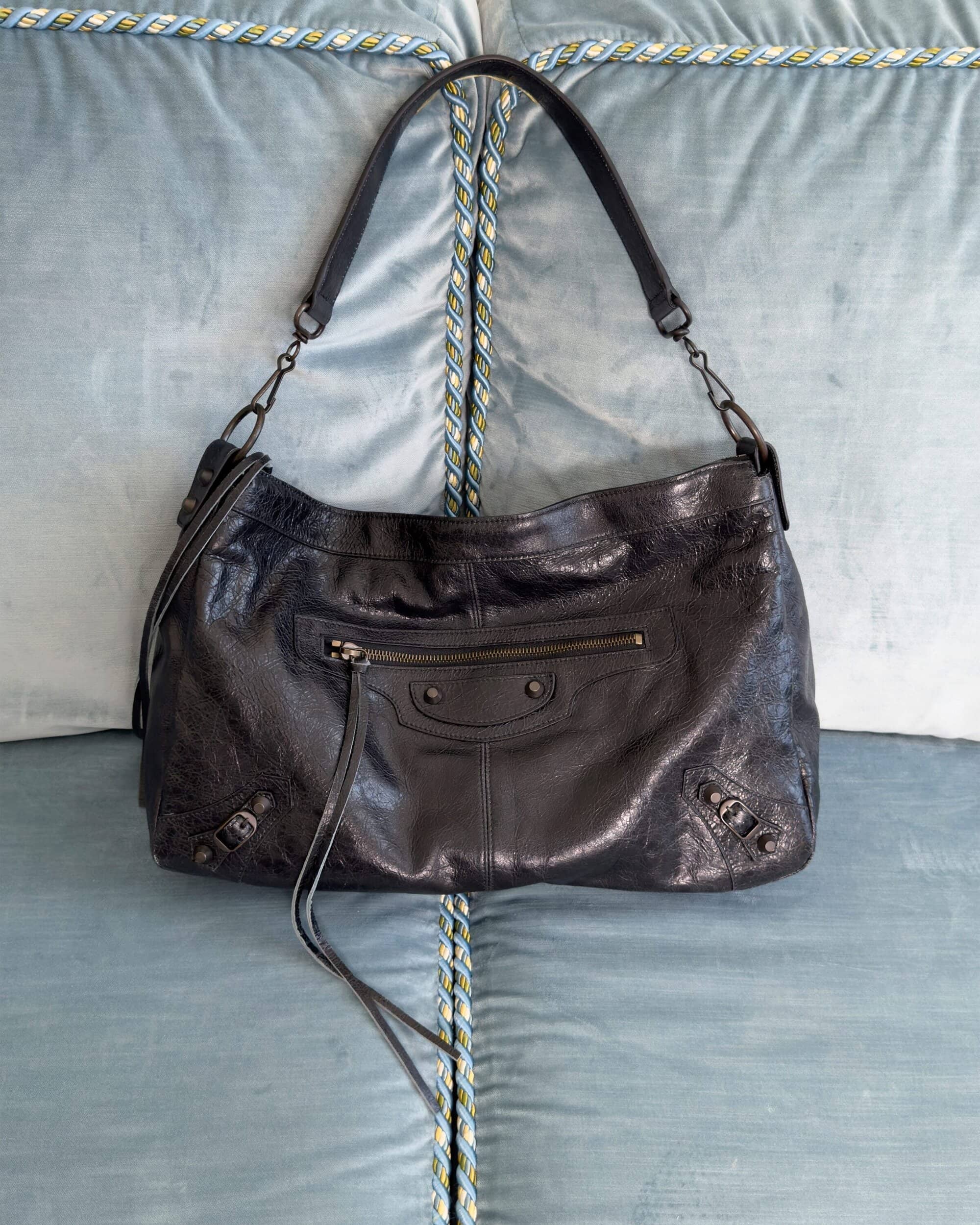 Black leather shoulder handbag with zipper pocket and straps resting on a blue tufted upholstered surface