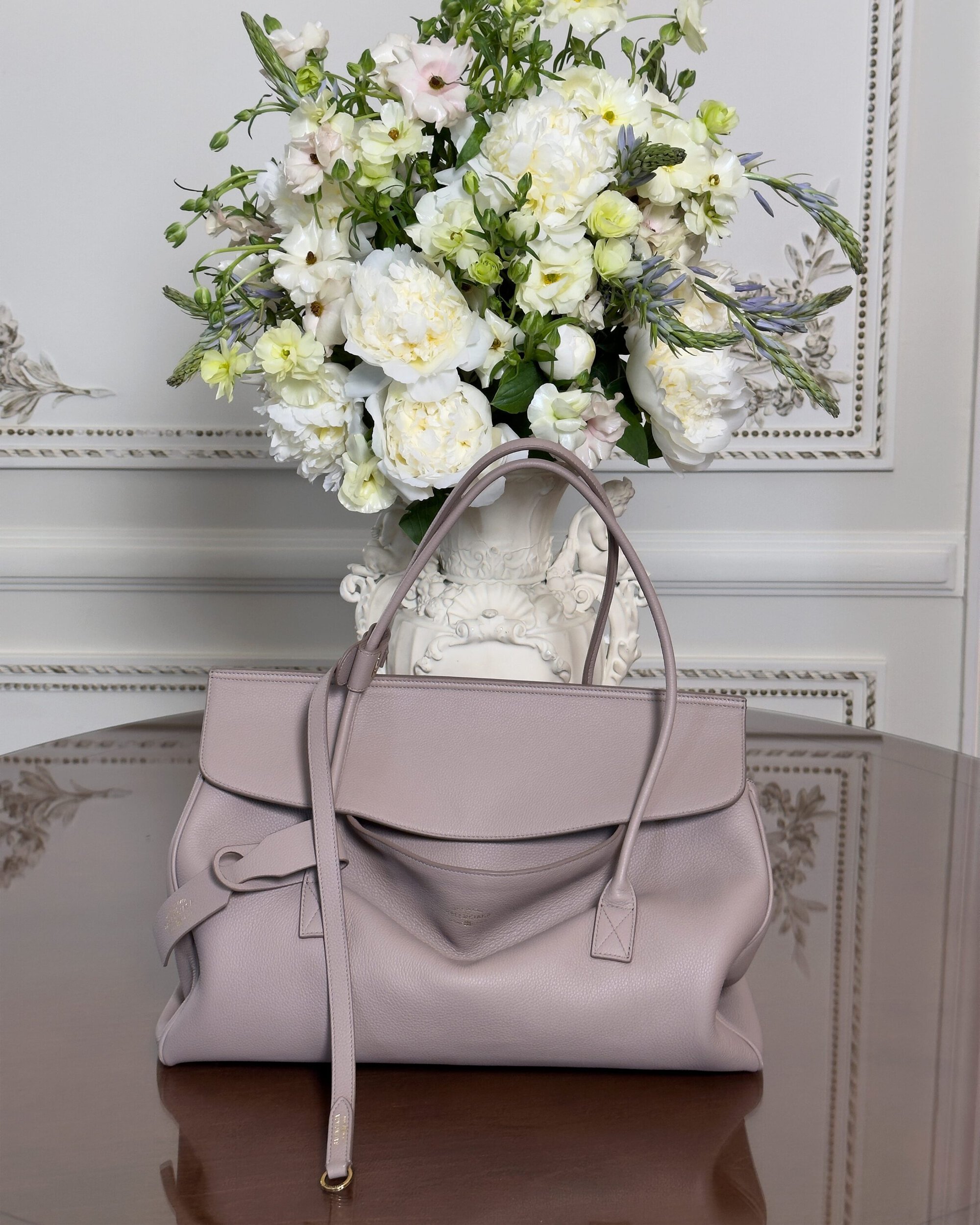 Balenciaga leather handbag on a dark polished table with white floral arrangement in background