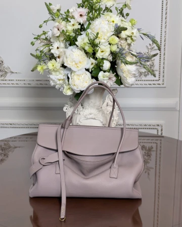 Balenciaga leather handbag on a dark polished table with white floral arrangement in background