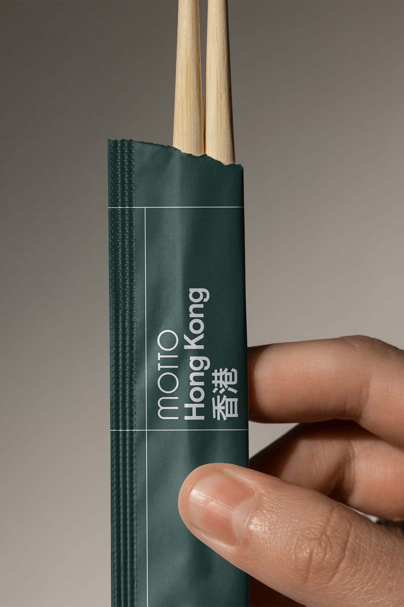 Hand holding a dark green paper chopstick sleeve featuring branded white typography against a neutral background