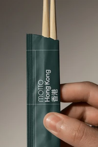 Hand holding a dark green paper chopstick sleeve featuring branded white typography against a neutral background