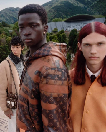 Three models outdoors in a landscape setting wearing designer apparel and carrying patterned bags for a fashion campaign.