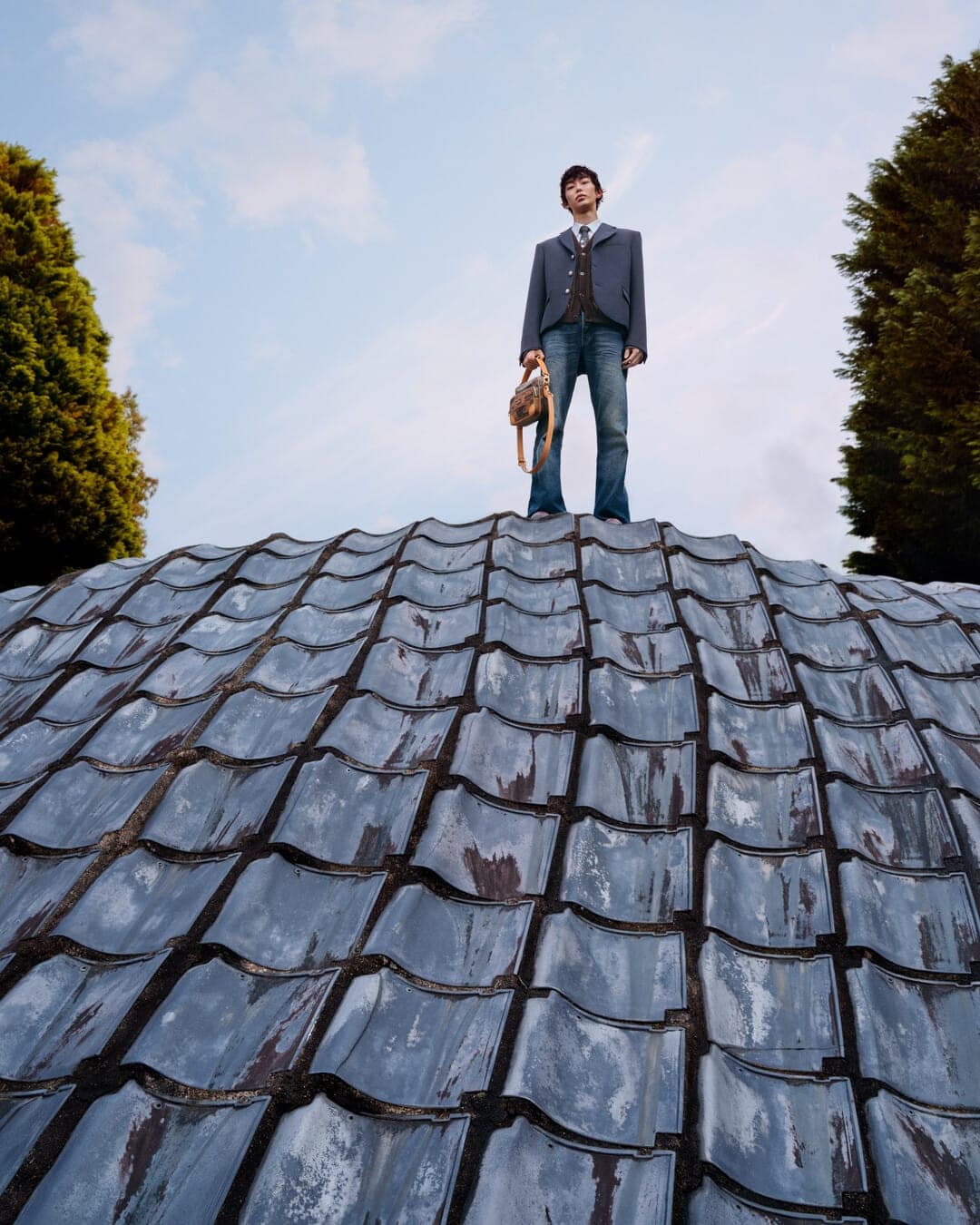 Man standing on a curved textured roof holding a handbag against a blue sky for Louis Vuitton