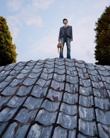 Man standing on a curved textured roof holding a handbag against a blue sky for Louis Vuitton