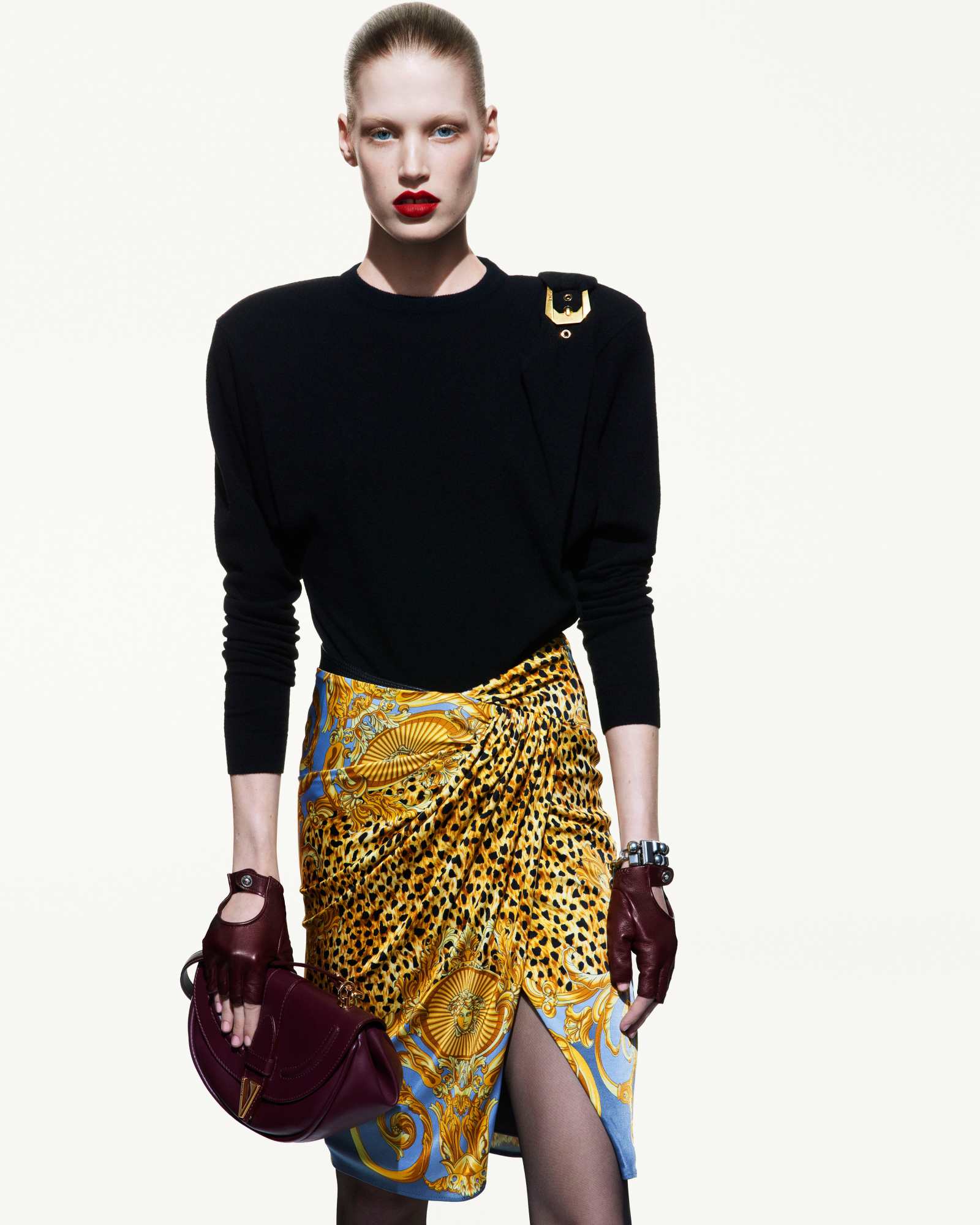 Model wearing a black top and patterned skirt with dark gloves against a white seamless background for Versace.