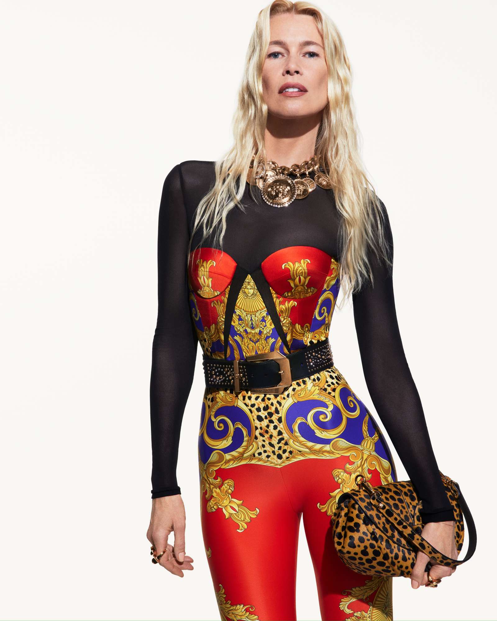 Claudia Schiffer wearing a Versace printed bodysuit with a statement necklace holding a leopard print handbag against a white background