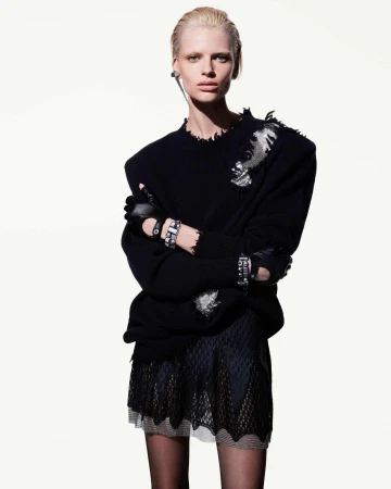 Model wearing a black distressed sweater and sheer patterned skirt against a plain white studio background
