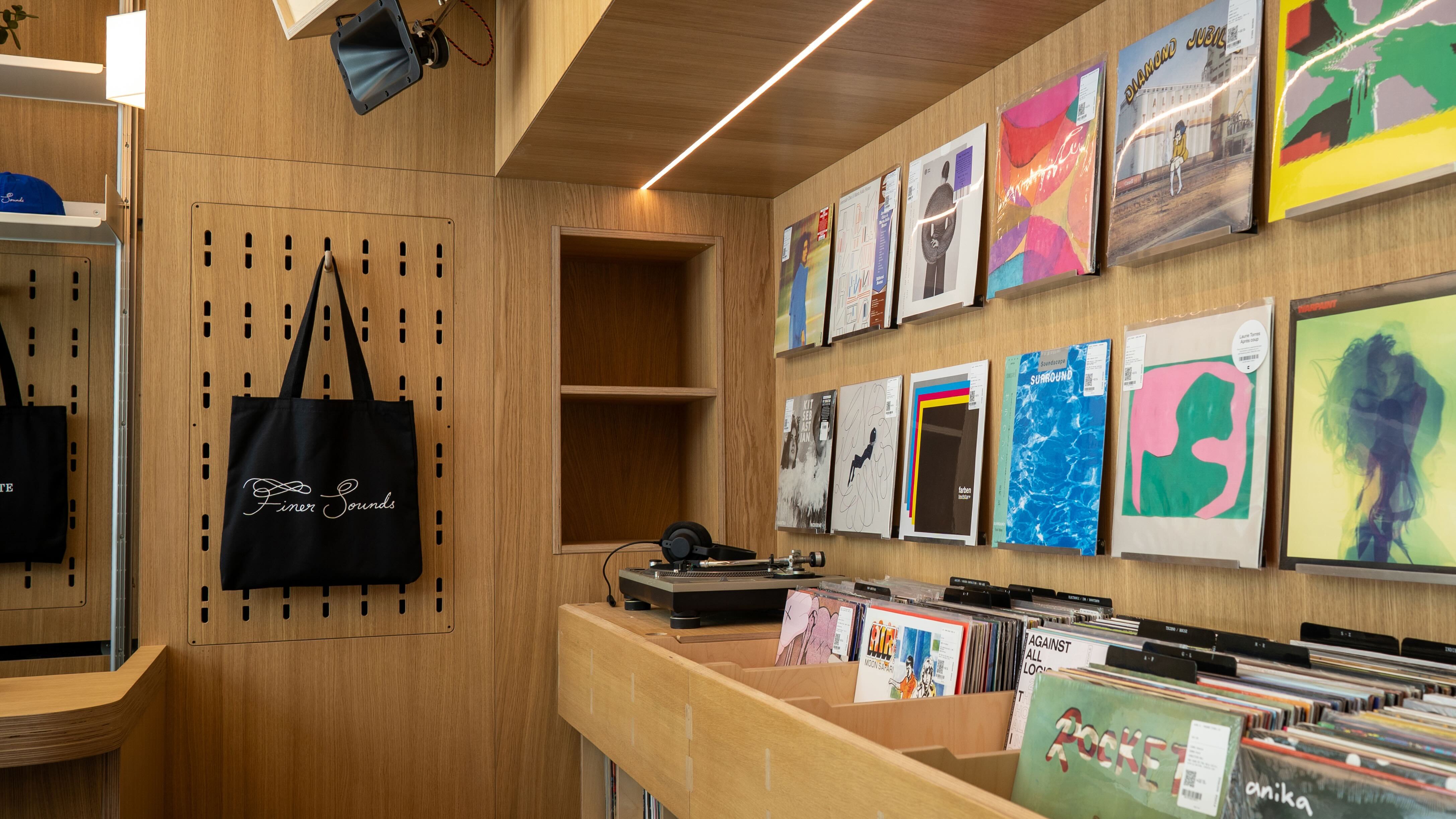 Interior of Finer Sounds record shop featuring wooden walls, display bins filled with vinyl records, and a black tote bag hanging on a pegboard.