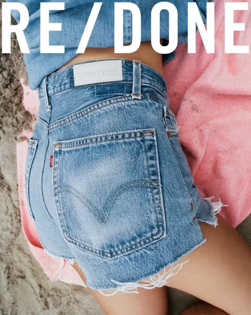 Close-up of denim shorts worn by a model on a sandy beach with a pink towel