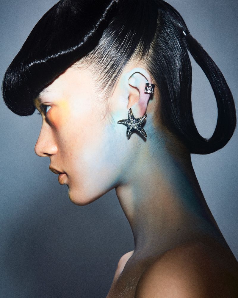 Profile shot of a woman with high-fashion black hair, dramatic star-shaped earring, and makeup with orange and blue face accents.