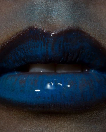 Close-up of a person's glossy, dark blue lips, set against a neutral skin tone, highlighting the rich color and texture of the makeup.