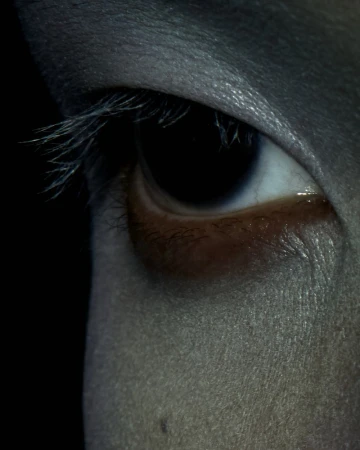 Close-up shot of a human eye with long lashes, detailed skin texture, and intense lighting, set against a dark background.