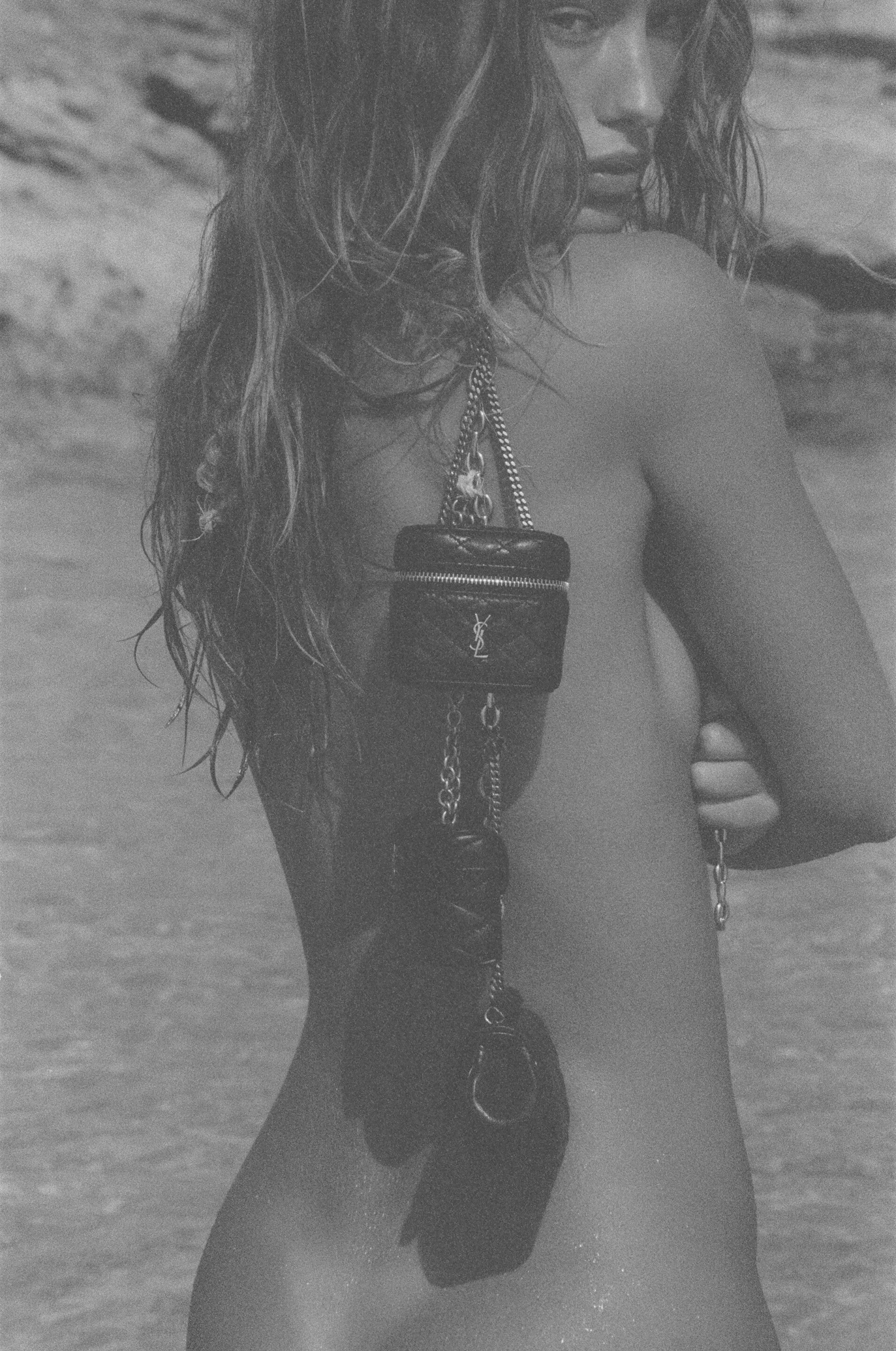 Monochrome portrait of a model draped with a small quilted black leather handbag, photographed by Henrik Purienne for Saint Laurent.