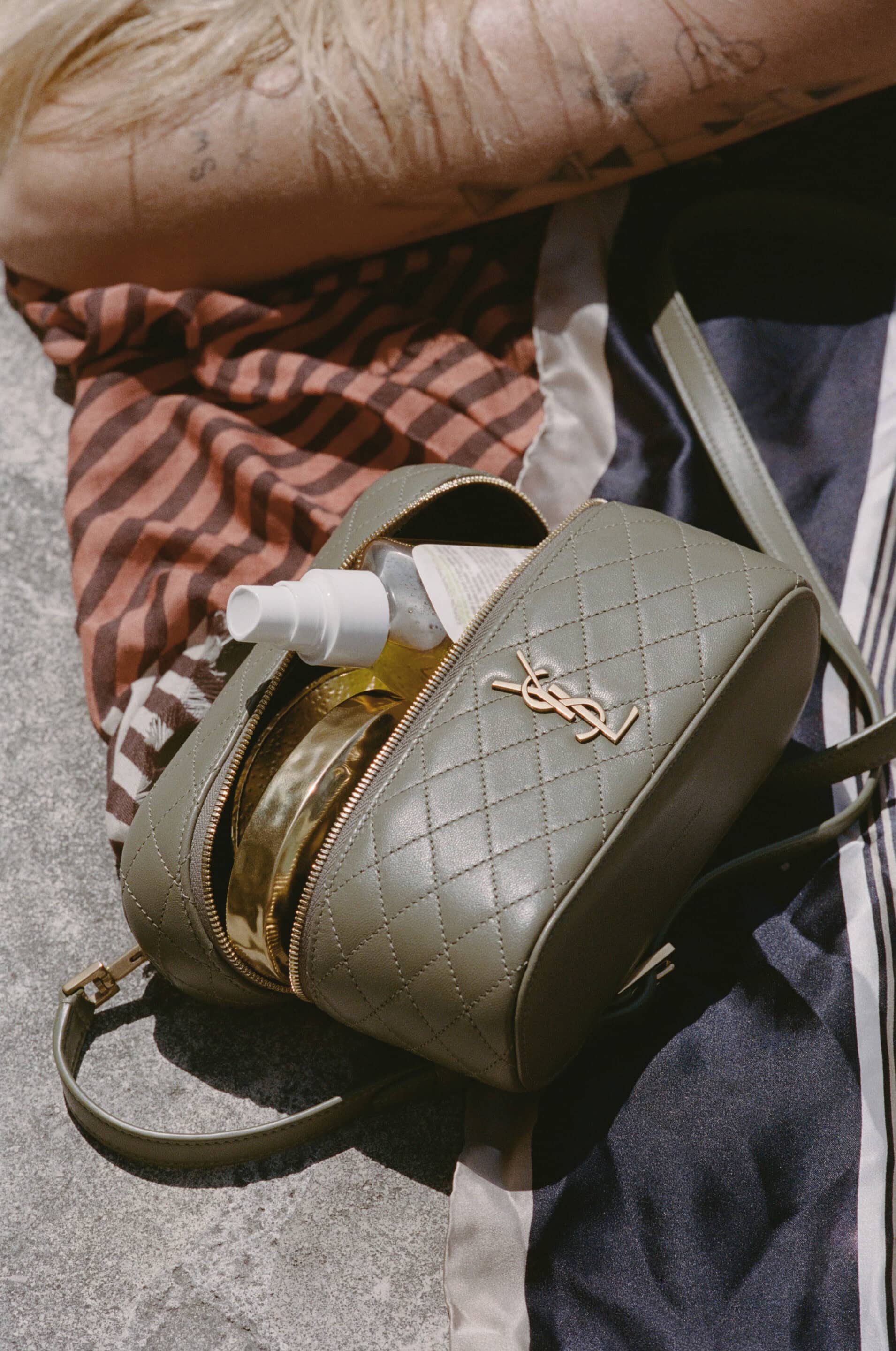 Quilted olive green Saint Laurent camera bag resting on patterned fabric and stone outdoors in sunlight.