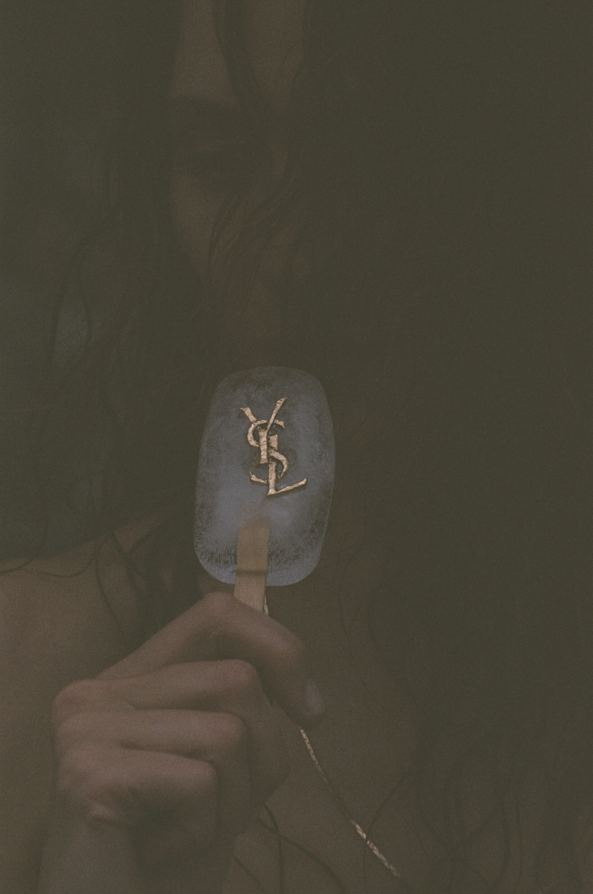 Close-up of a person holding an ice pop embedded with a gold YSL logo for Saint Laurent.