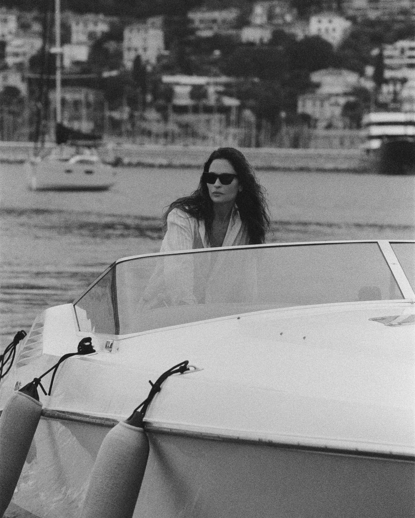 Woman in sunglasses on a speedboat in front of a coastal town
