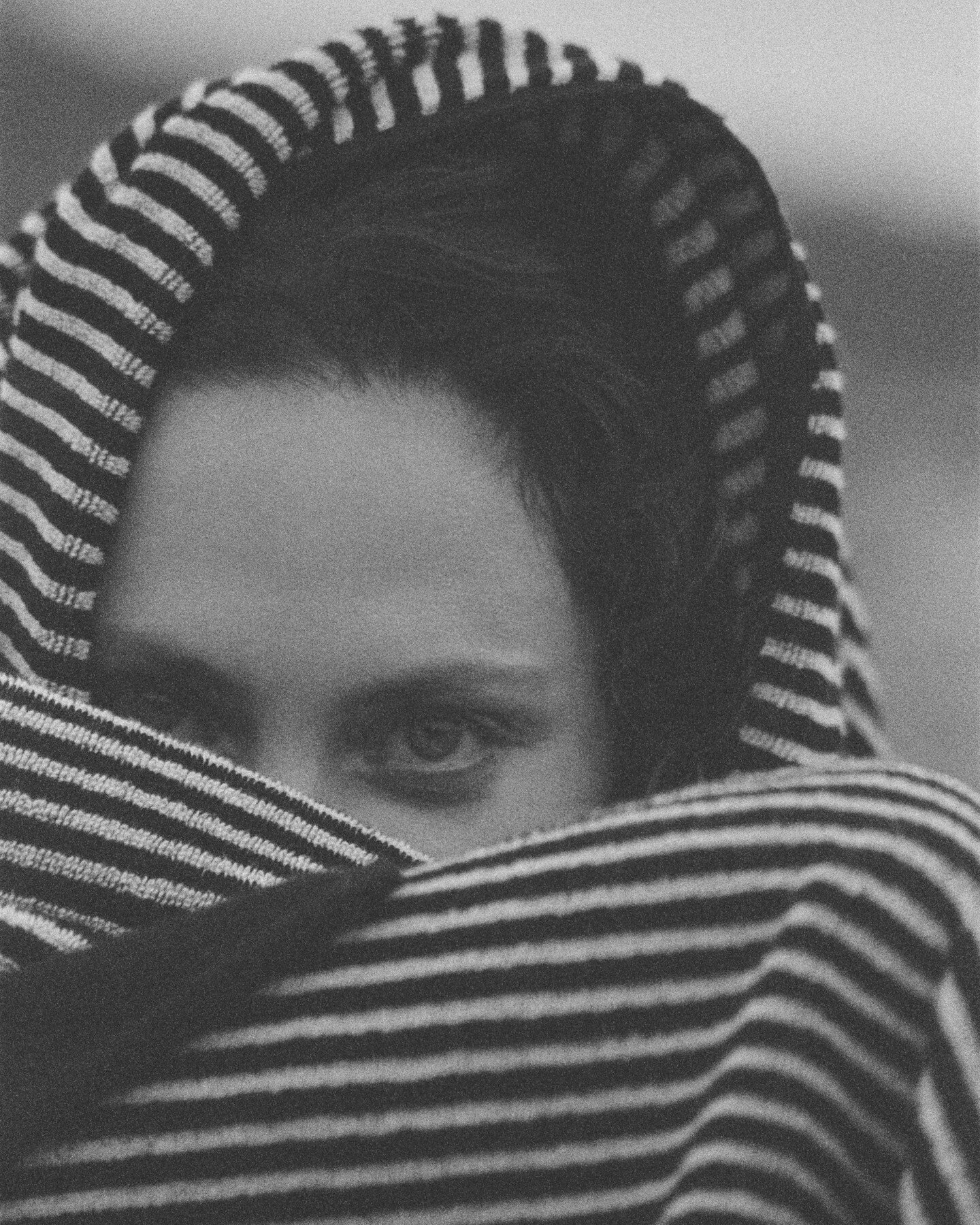 Close-up of a woman's face wrapped in a black and white striped towel, revealing only her eyes.