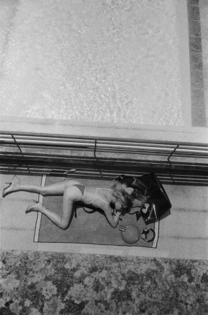 Overhead black and white photo of a model in a swimsuit crawling on a towel by a pool for Saint Laurent.