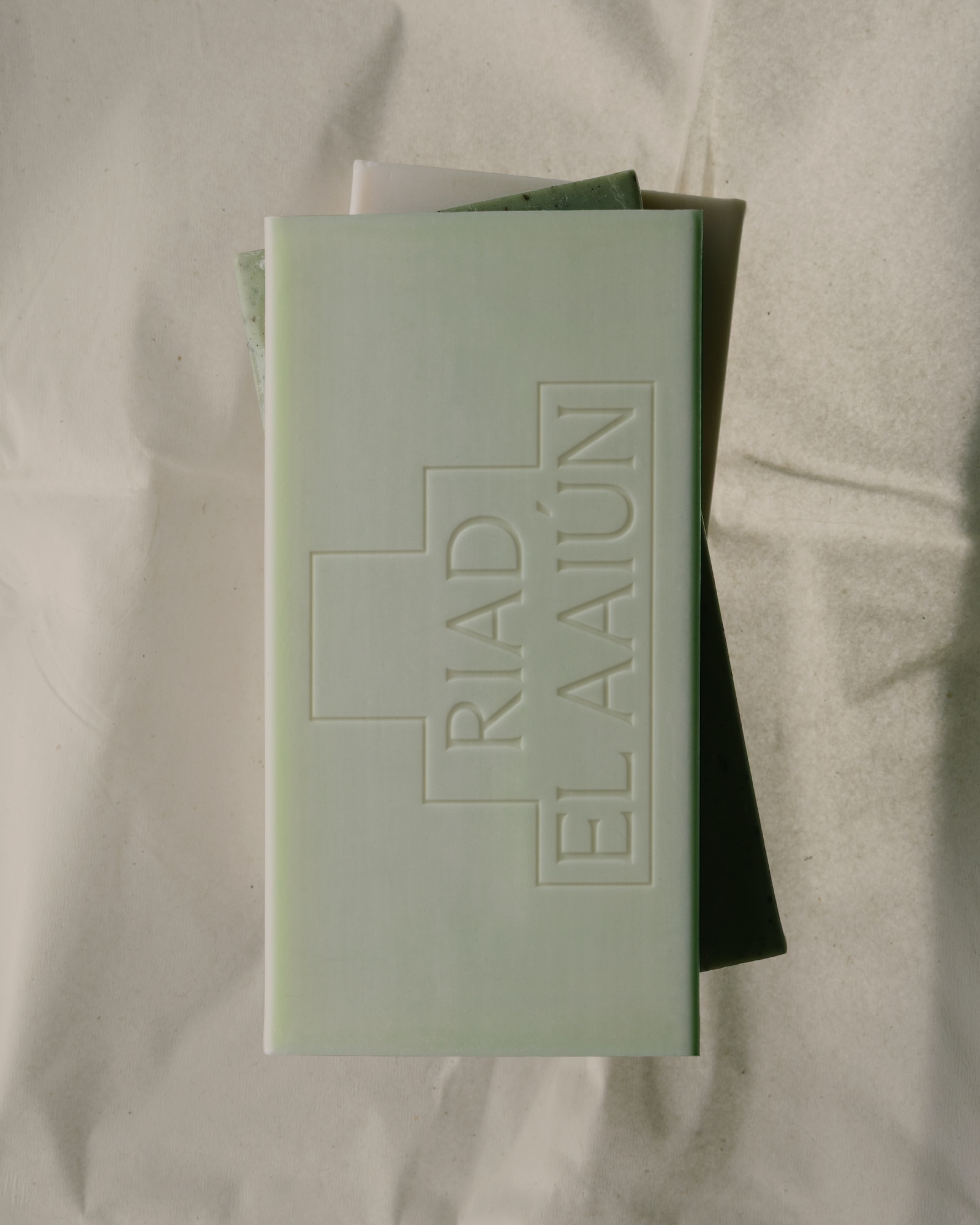 Green embossed soap bar resting on crumpled white paper packaging for Riad El Aaiün brand identity