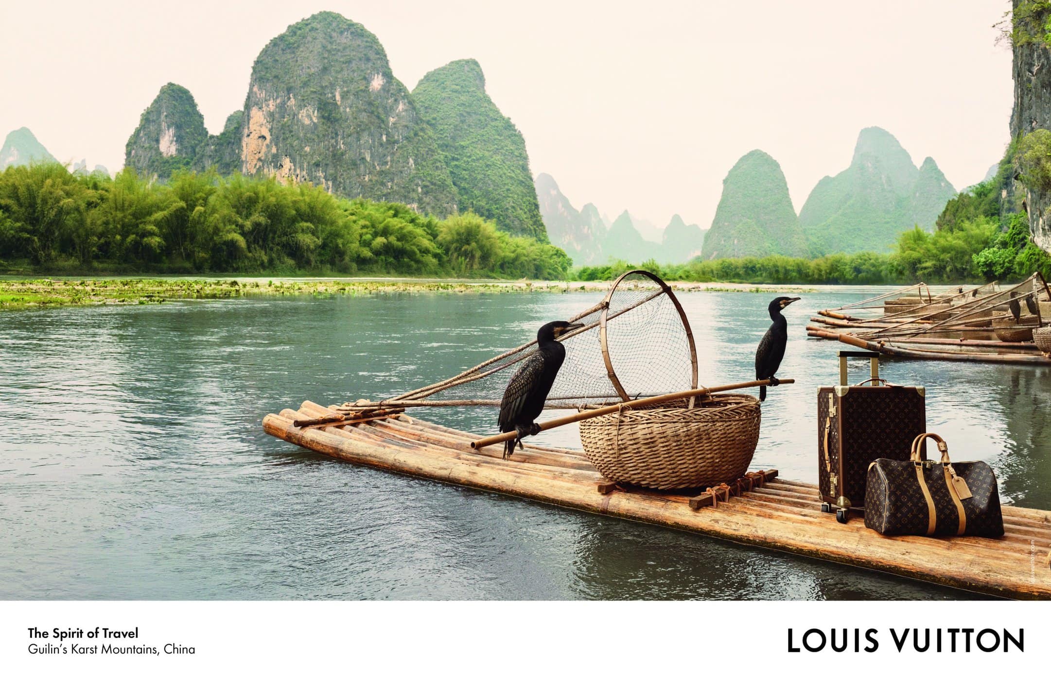 Louis Vuitton luggage on a bamboo raft with cormorant birds floating on a river amid karst mountains in Guilin, China.