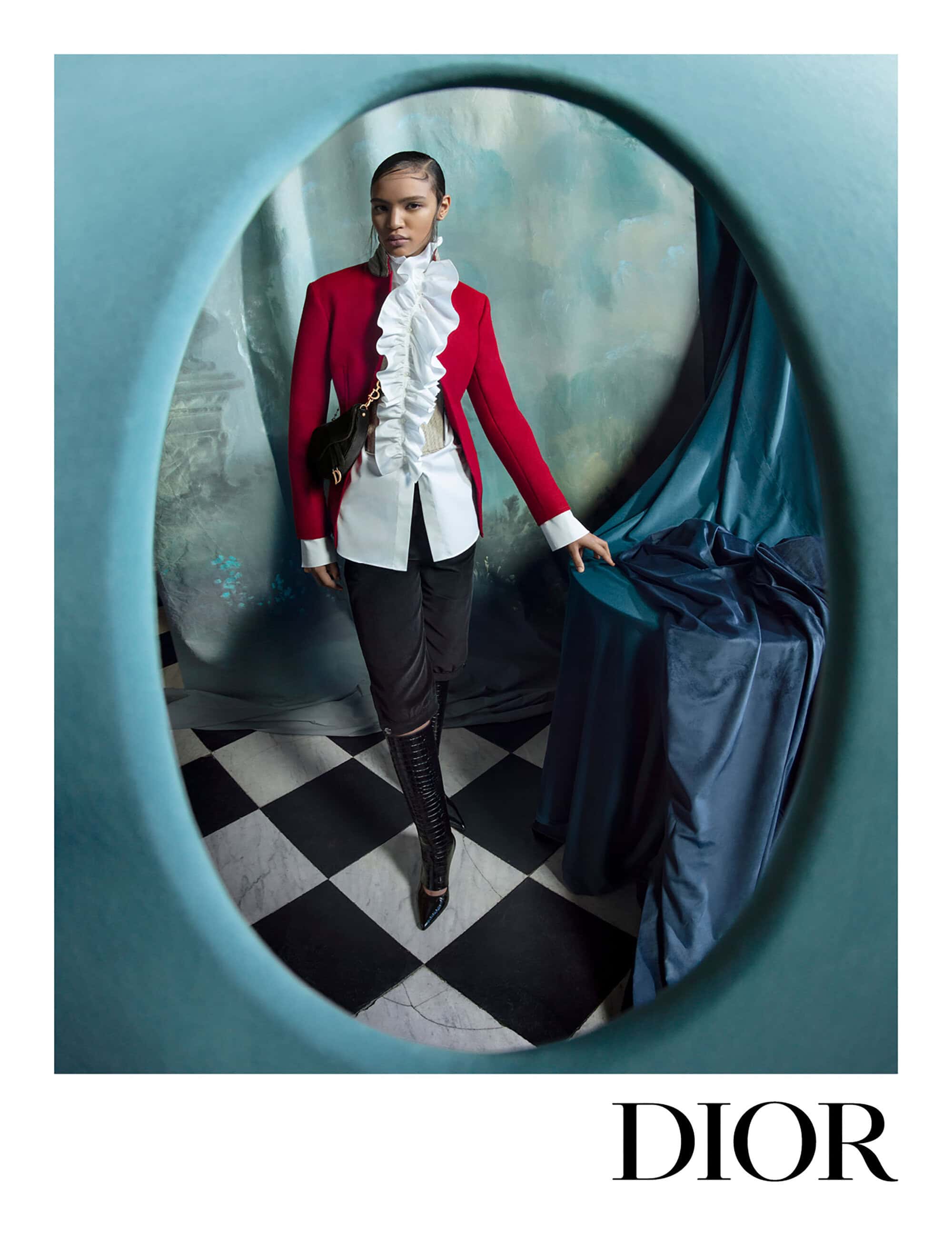 Model in red blazer and white ruffled shirt framed by a teal oval aperture over a checkered floor