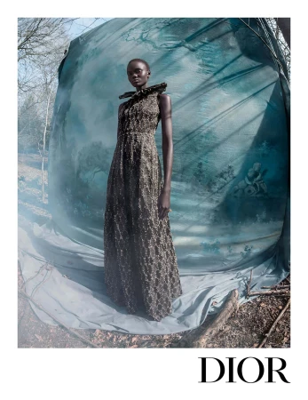 Model wearing a dark textured gown standing in front of a draped teal painted backdrop outdoors.