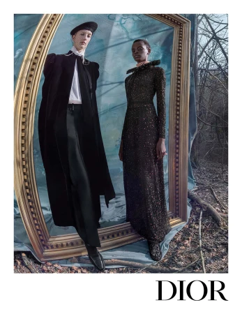 Two models posing inside a large ornate golden frame set outdoors among trees for the Dior Fall 2025 ad campaign.