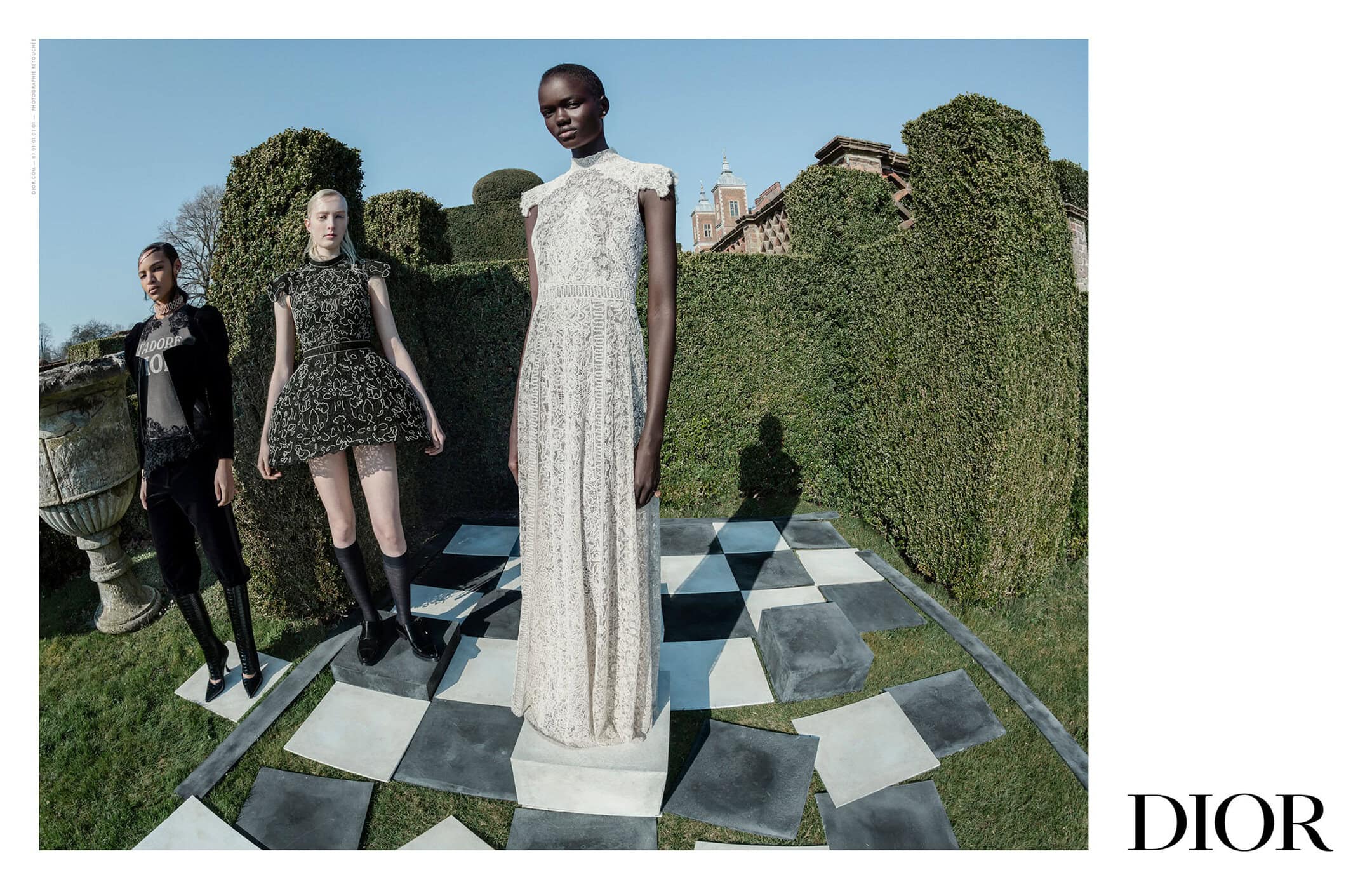 Three models wearing Dior designer fashion posing on a stone chessboard platform in a formal garden