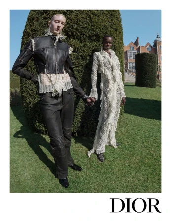 Two models standing on a lawn holding hands in front of a topiary hedge, wearing Dior fall 2025 campaign apparel