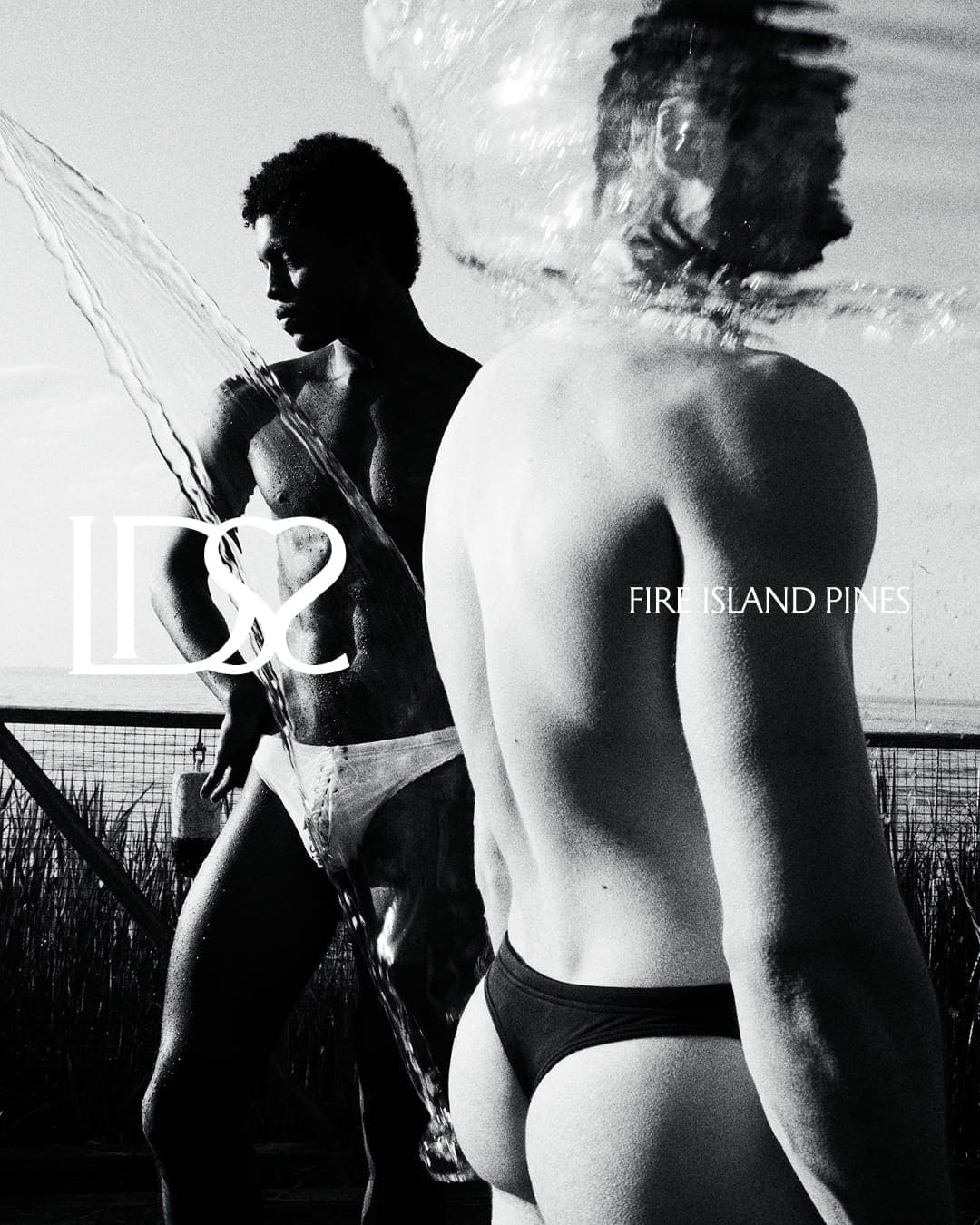Black and white swimwear ad campaign image featuring two male models outdoors with splashing water and text overlays
