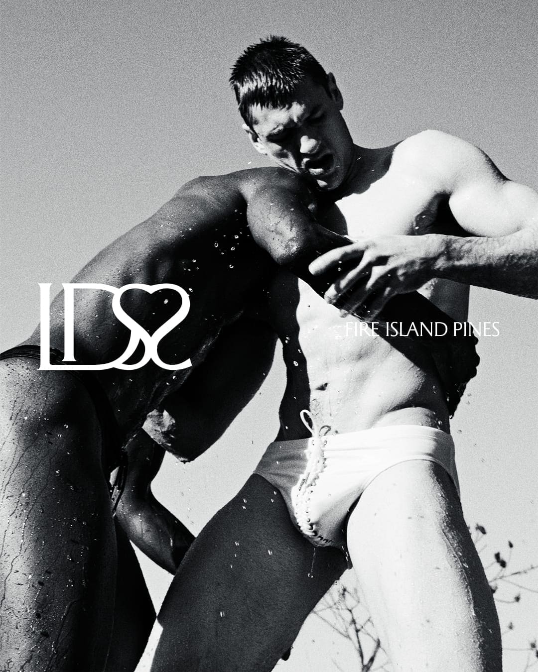 Two men wrestling outdoors in swimwear, water splashing against their skin under bright sunlight, captured in a dynamic black and white composition.