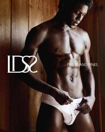 Shirtless black man wearing white lace-up briefs standing against vertical wood paneling for Ludovic de Saint Sernin