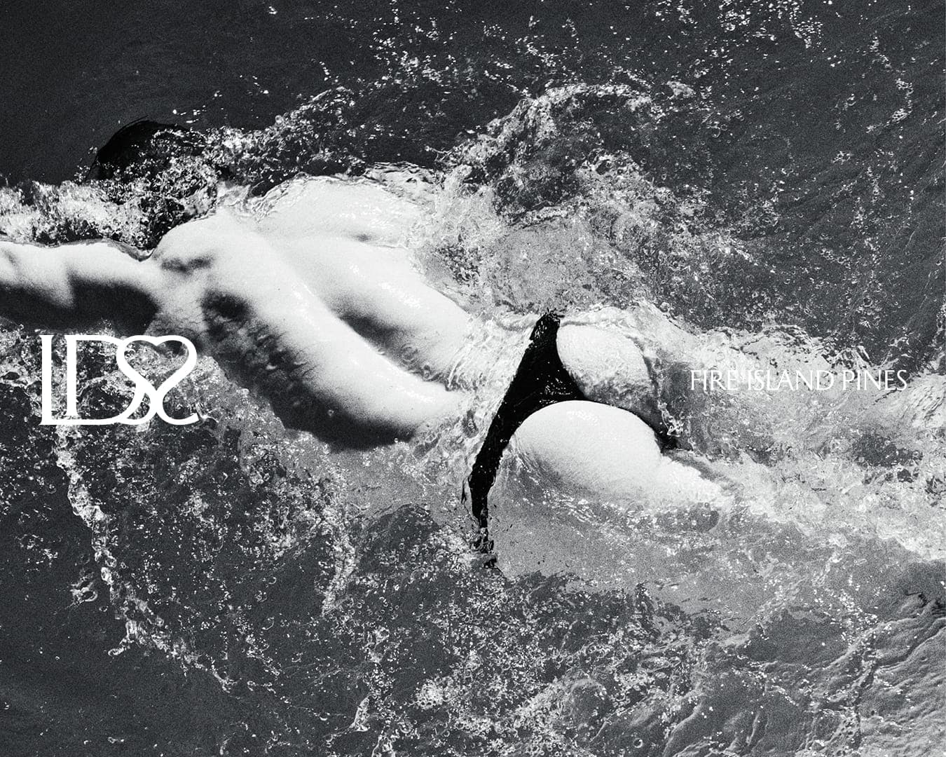 Black and white image of a person swimming in water, wearing dark briefs, with splashing water surrounding them.