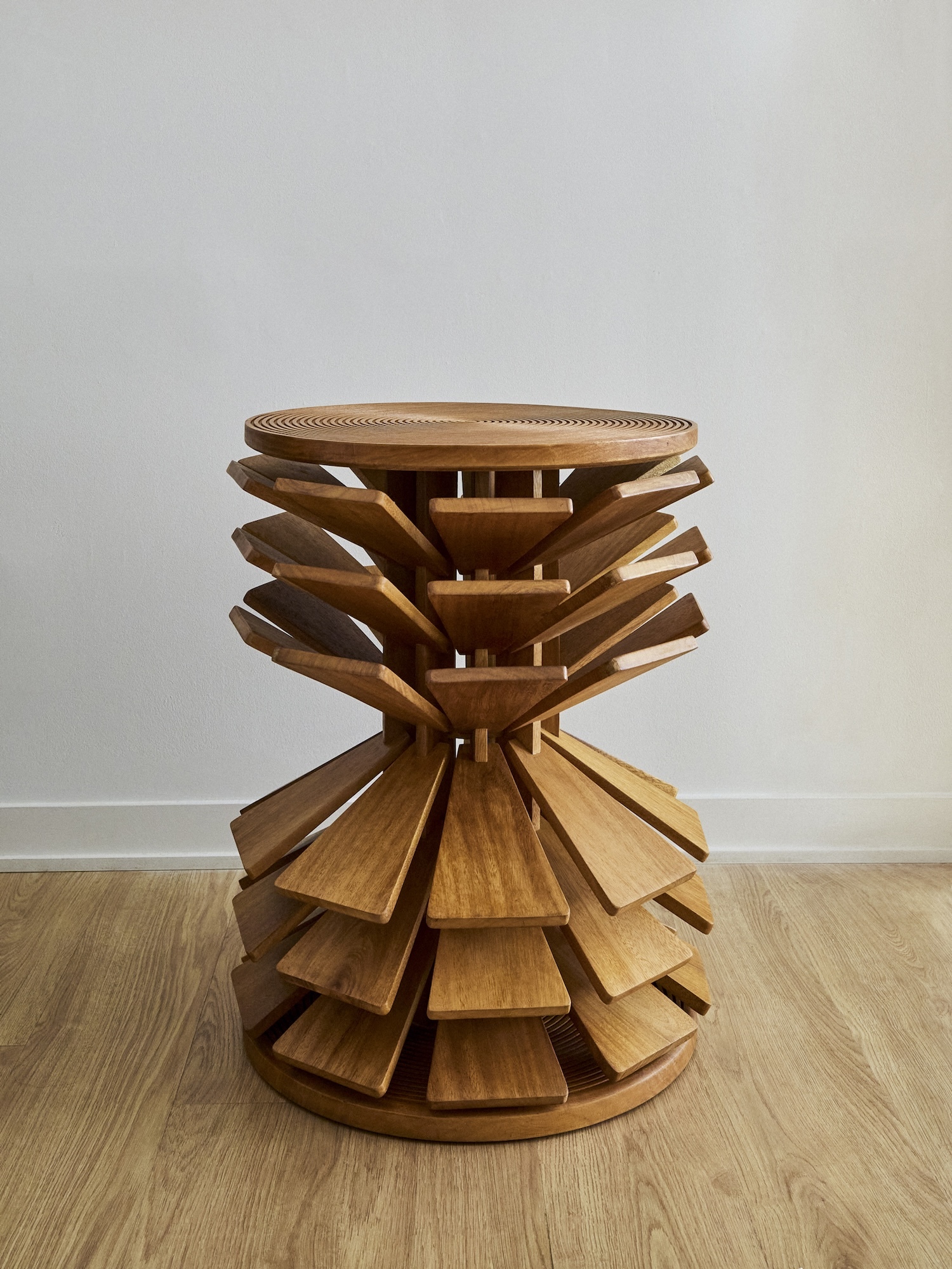 Sculptural wooden stool with radial fin design set against a pale wall and wooden floor for Hello Human and Lyle Gallery brand identity.