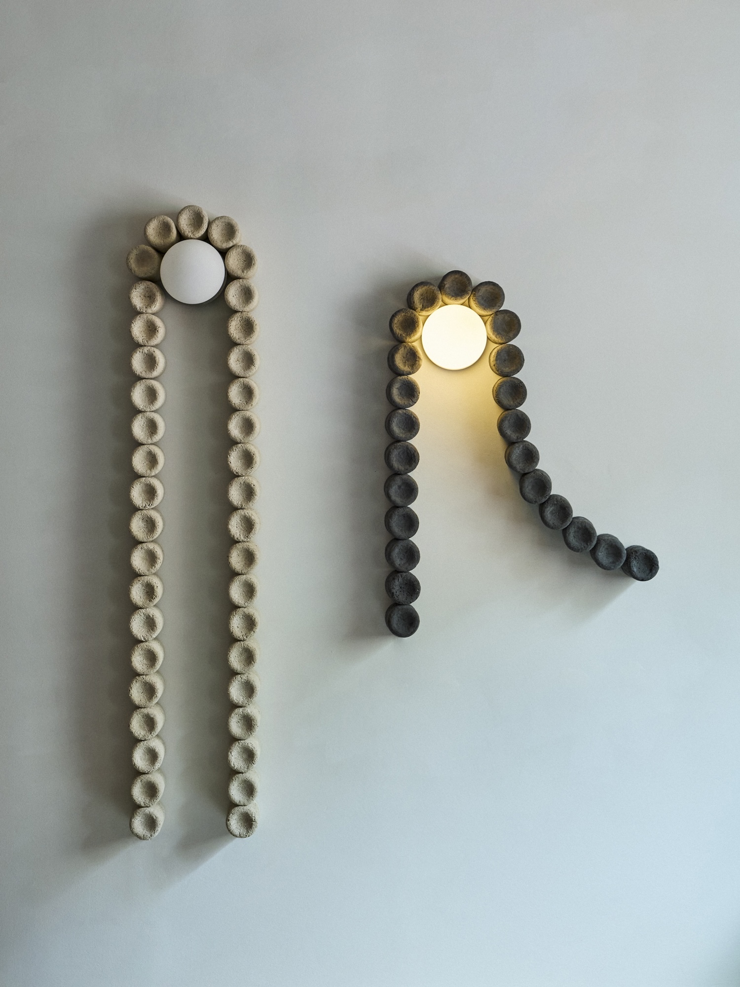 Two sculptural wall lamps made of textured modular units mounted on a plain neutral wall.