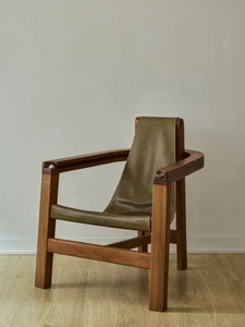 Wooden armchair with an olive green leather sling seat and backrest positioned against a pale wall.