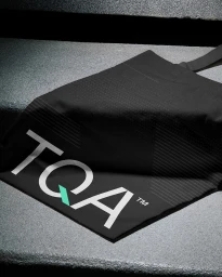 Black fabric bag with TQA logo resting on a textured concrete step surface.