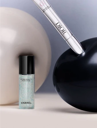 Cosmetic still life with Chanel Hydra Beauty Micro Serum and Dior concealer set against neutral and black sphere backgrounds.