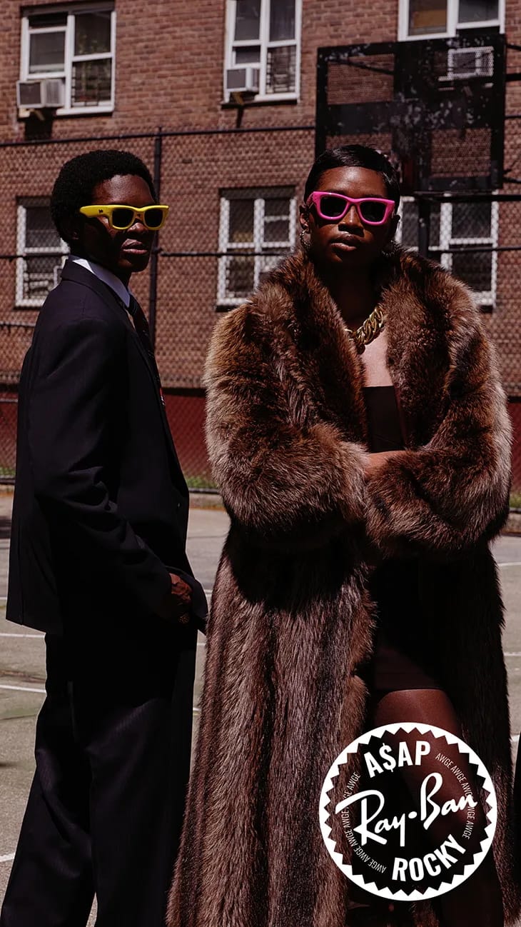 Two models posing outdoors against a brick building, featuring a brown fur coat and yellow and pink sunglasses.