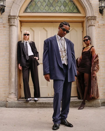 A$AP Rocky wearing sunglasses and an oversized blue suit standing outdoors with two models in front of a building exterior.