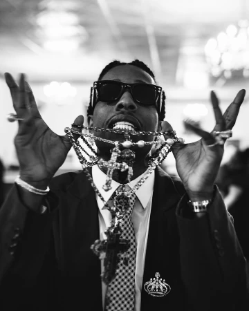 A$AP Rocky in a dark suit wearing sunglasses and holding multiple layered cross necklaces in the Ray-Ban advertising campaign.