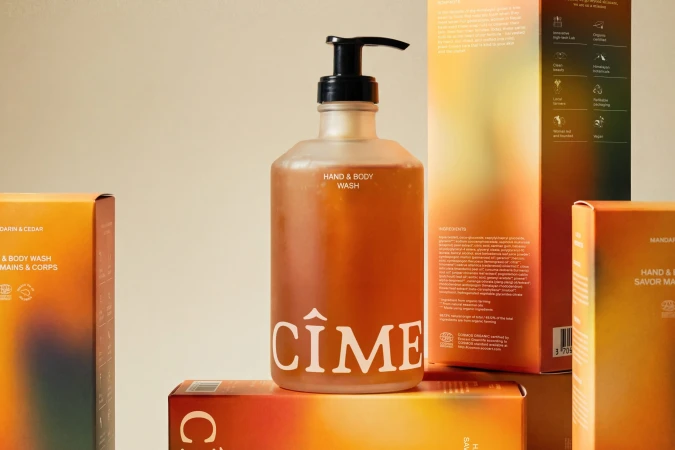 Frosted glass pump bottle of CIME hand and body wash surrounded by gradient-coloured product packaging boxes